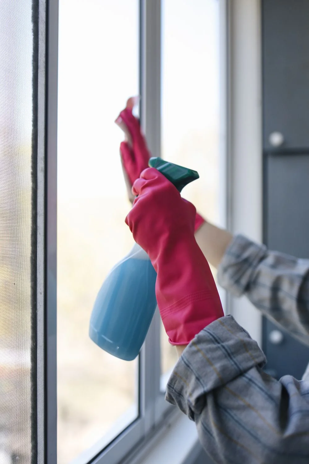 Eine behandschuhte Hand reinigt eine Glasfläche – Symbolbild